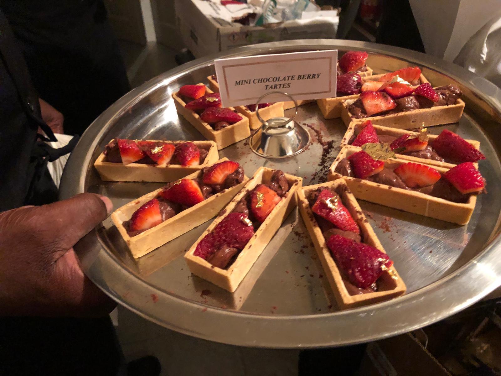 Tray of mini chocolate berry tartes topped with strawberries and gold leaf